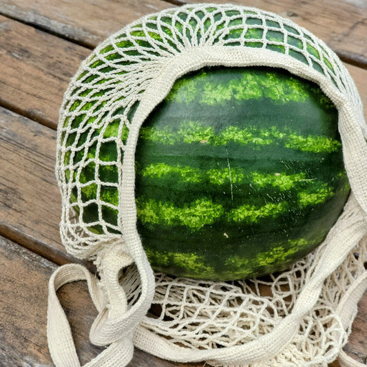 Watermelon in a beige mesh bag on a wooden surface