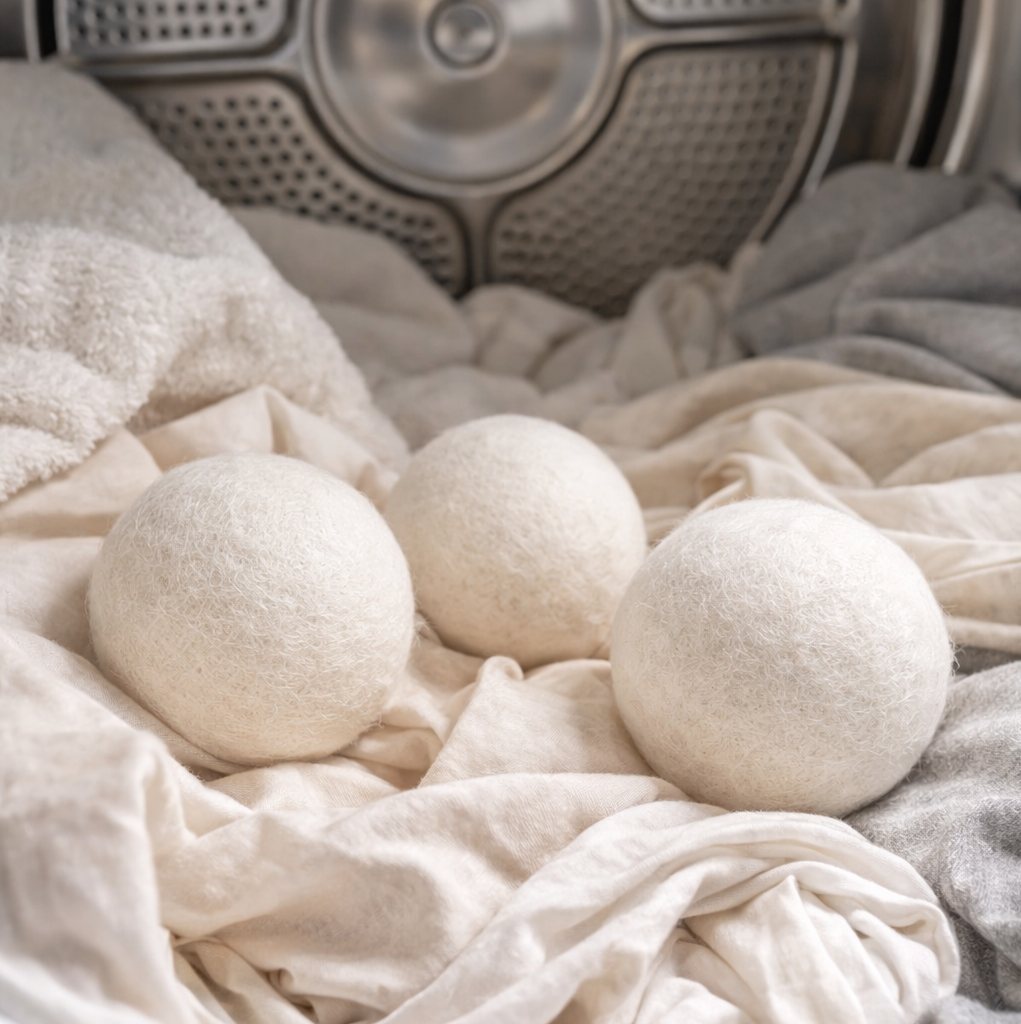 Three white dryer balls on a pile of clothes with a dryer in the background.