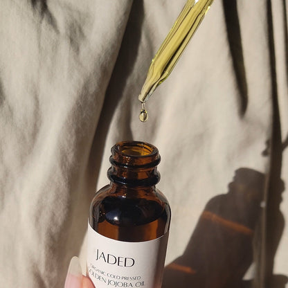 Hand holding a bottle of Jaded jojoba oil with a dropper, against a neutral background.