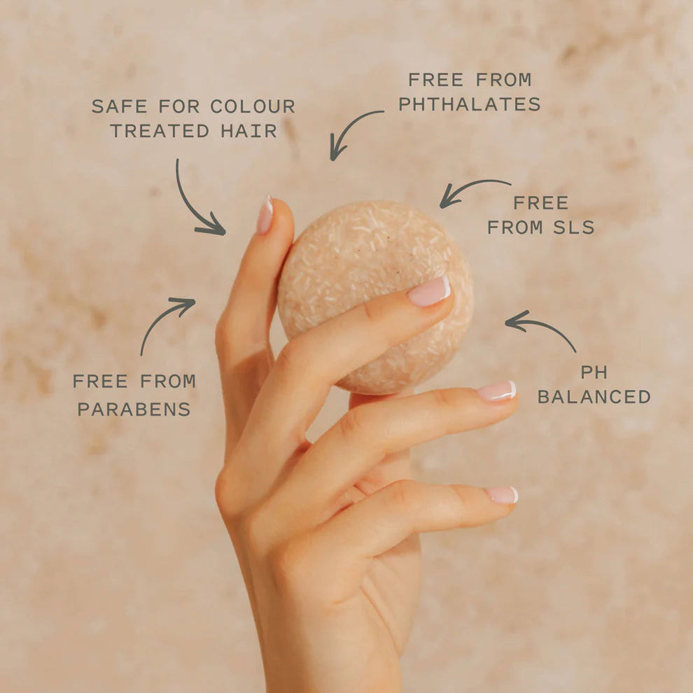 Hand holding a volumizing shampoo bar with text indicating its benefits on a beige background