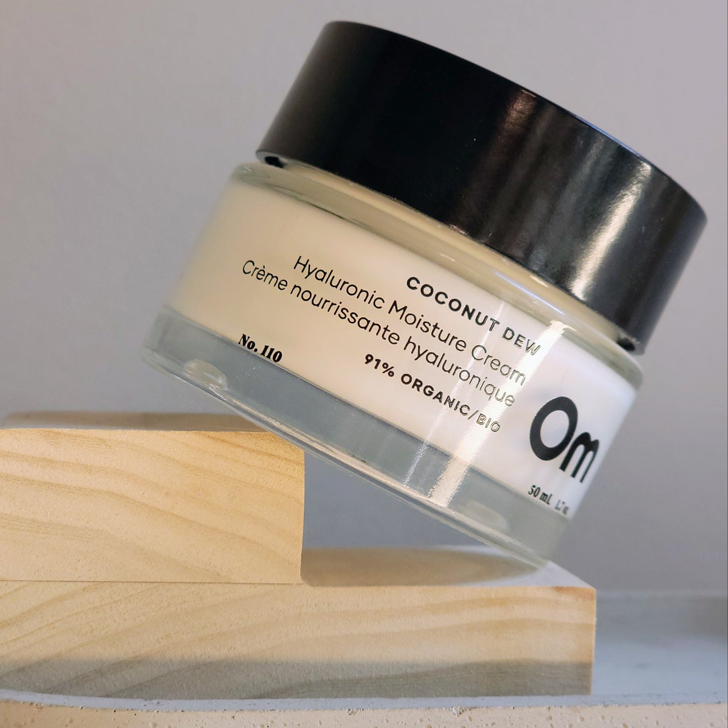 Jar of coconut-derived hyaluronic moisture cream on a wooden stand with a gray background