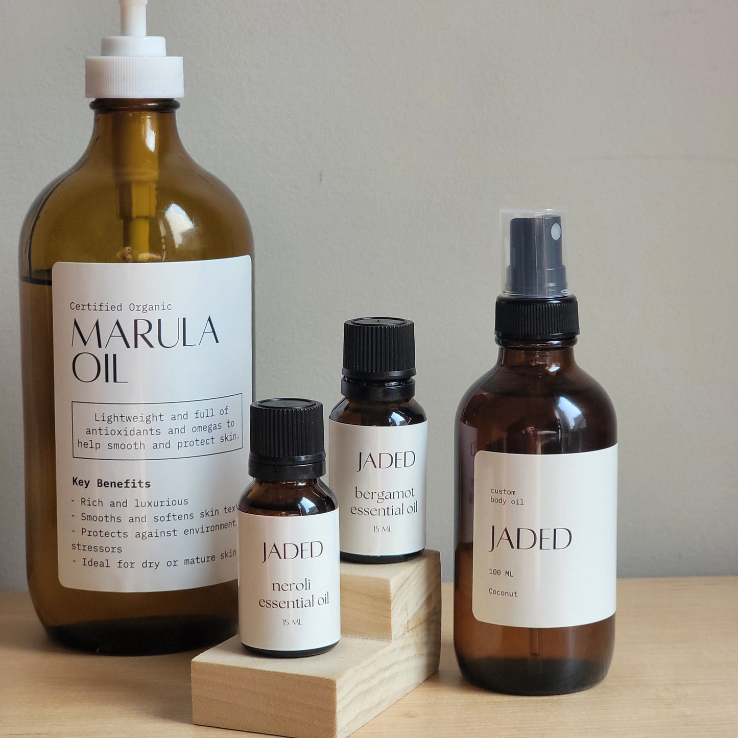 Collection of Jaded body oil, essential oils and Marula oil bottles on a wooden block with a neutral background