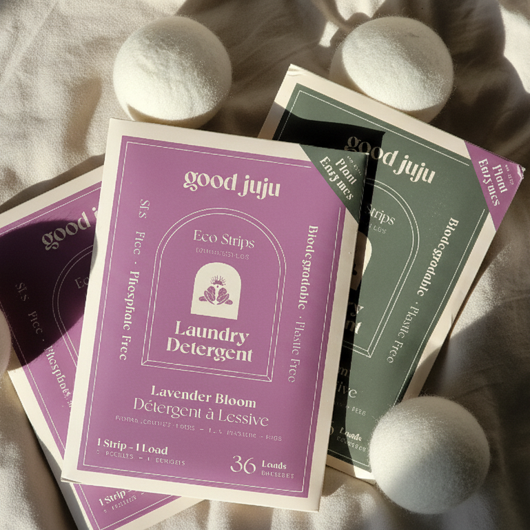 Good Juju laundry detergent packets on a textured surface with dryer balls.